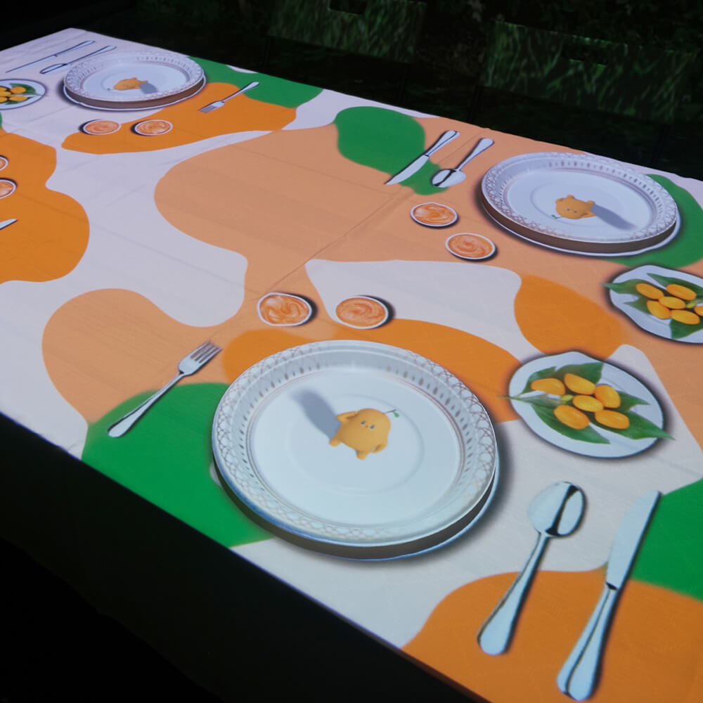 An innovative dining experience where colorful, organic patterns are projected directly onto the table surface around plates and utensils. The dynamic visual display transforms the meal into an artistic experience, with flowing shapes in orange, green, and white creating an ever-changing tableside canvas.